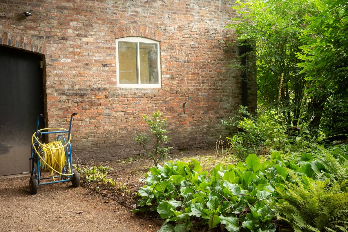 A neatly mounted gardening water hose reel on a shed wall with a coiled green rubber hose